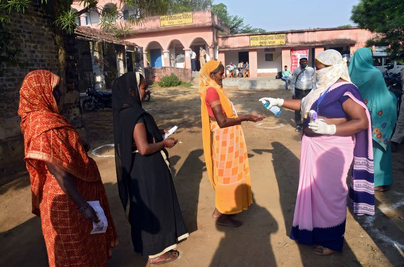 A woman sprays sanitizer on a voter's hand as she and others wait in a queue to cast their vote outside a polling booth during the state assembly election, at a village on the outskirts of Patna