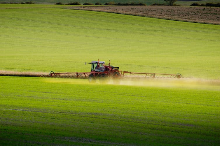 A tractor with outspread spraying arms in a field.