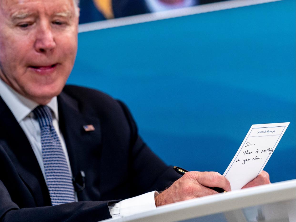 President Joe Biden holds a card handed to him by an aide that reads 
