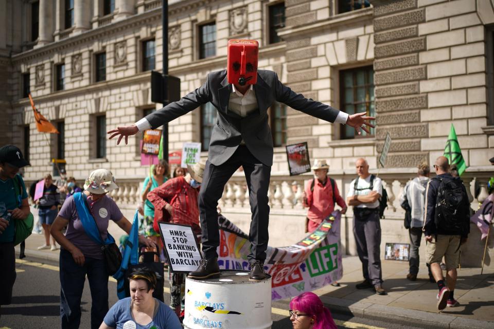 A man wearing a petrol on top of a barrel joins climate activists from XR during a protest outside the offices of HM Revenue and Customs (HMRC) (PA)