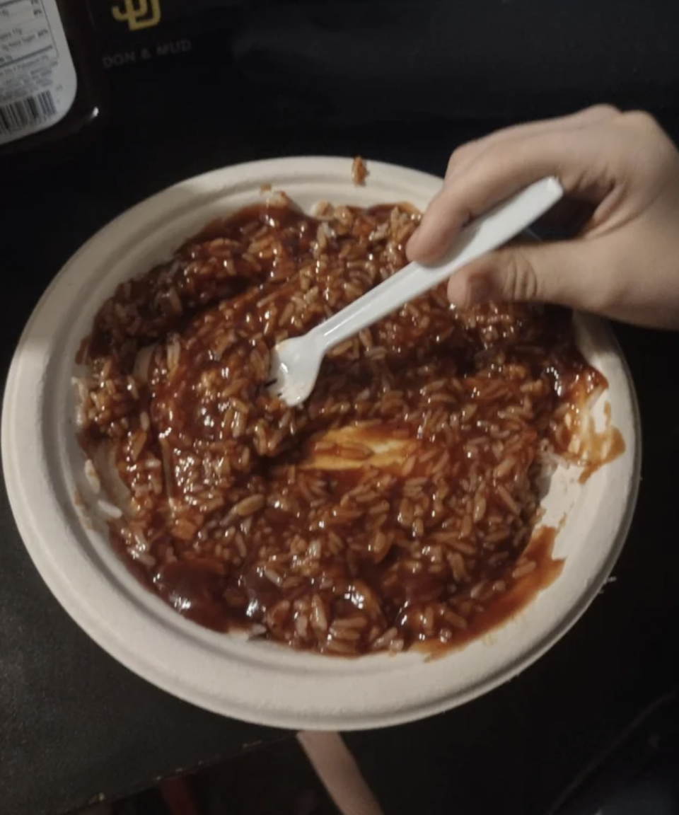 A person is eating rice drenched in BBQ sauce