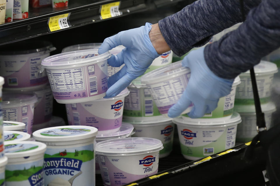 FILE- In this March 24, 2020 file photo, a woman reaches for yogurt wearing gloves during senior shopping hours at Homeland in Oklahoma City. To avoid any traces of the coronavirus that might be lurking on surfaces, Americans have been wiping down groceries, wearing surgical gloves in public and leaving mail packages out for an extra day or two. But experts say fear of being infected by touching something can be overblown. (AP Photo/Sue Ogrocki, File)