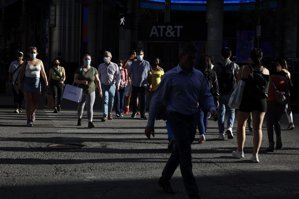 Evening light falls on pedestrians and shoppers as they cross the street in downtown Chicago, Wednesday, May 26, 2021. With vaccinations rolling out and shoppers freer to go out maskless, retailers are seeing an eager return to their stores after months of watching their customers focus on online buying during the pandemic. (AP Photo/Shafkat Anowar)