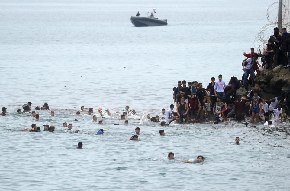 Moroccan citizens stand next to and swim around the fence between the Spanish-Moroccan border. (Reuters)