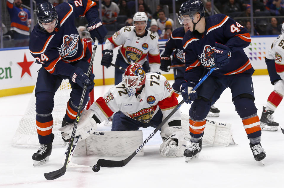 Florida Panthers goalie Sergei Bobrovsky (72) reaches for the puck between New York Islanders defenseman Scott Mayfield, left, and center Jean-Gabriel Pageau during the second period of an NHL hockey game Friday, Dec. 23, 2022, in Elmont, N.Y. (AP Photo/John Munson)