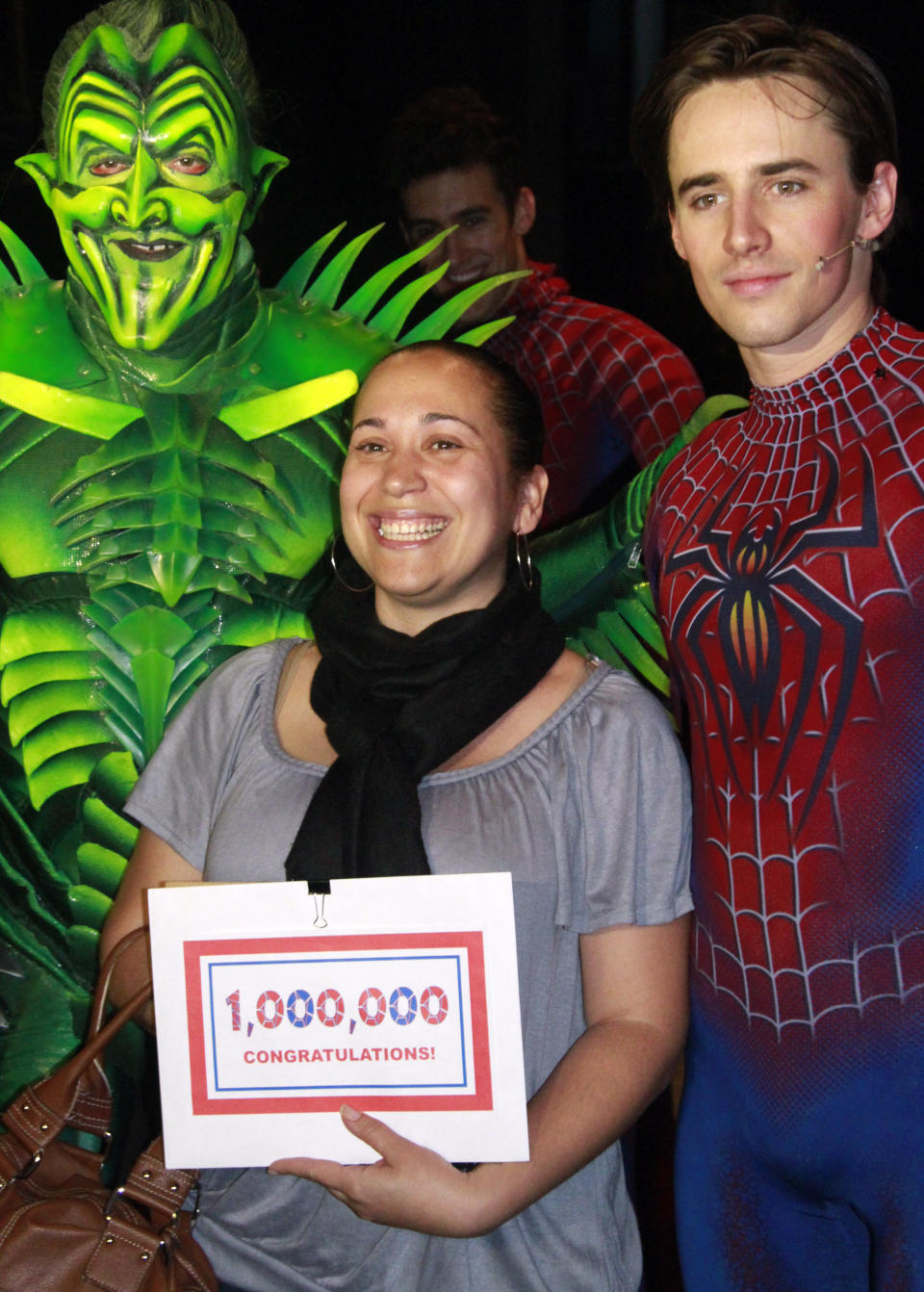 Yvelisse Fermin, from the New York City borough of Queens, poses with "Spider-Man Turn of the Dark" stars Patrick Page, left, as the Green Goblin, and Reeve Carney, as Spiderman, after she is awarded a city tour package as the one millionth viewer of the production on Wednesday, May 16, 2012, in New York. (AP Photo/Bebeto Matthews)