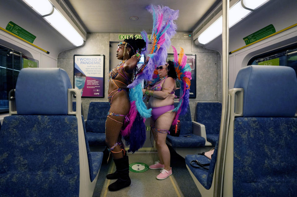 Missy, right, fixes her friend Sasha's costume as they ride the train to the Caribbean Carnival parade in Toronto, Canada, Saturday, July 30, 2022. The 55th annual parade returned to the streets after the COVID-19 pandemic cancelled it for two years in a row. (AP Photo/Kamran Jebreili)