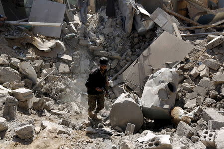 A police trooper walks in a creater caused by an air strike on houses near Sanaa Airport, March 31, 2015. REUTERS/Khaled Abdullah