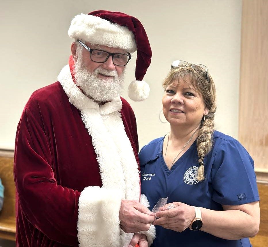 Santa Claus, also known as retired Wichita County Judge Woody Gossom, hands out a candy cane to county employee Dora Dehoyos during his annual yuletide rounds at the Wichita County Courthouse.