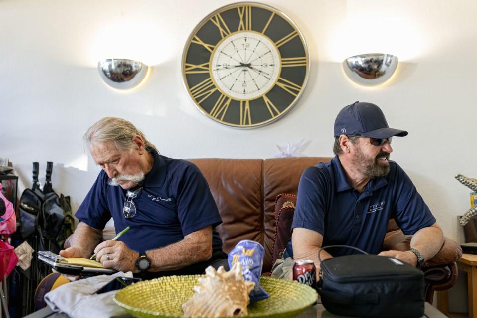 Two men sit on a couch with a clock behind