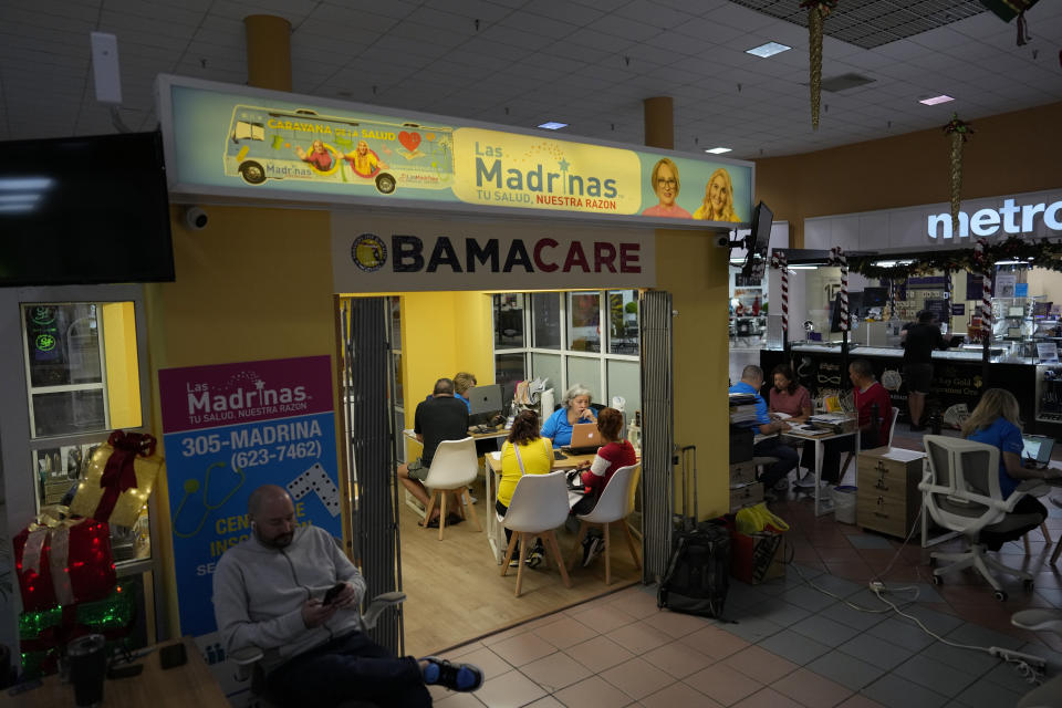 Insurance agent Maria Collado, center, works with clients at a shopping mall kiosk run by Las Madrinas de los Seguros, Spanish for "The Godmothers of Insurance," at a shopping center in Miami, Tuesday, Dec. 5, 2023. (AP Photo/Rebecca Blackwell)