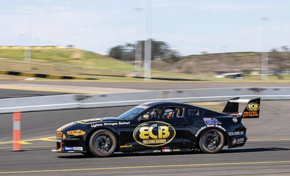 A black race car with sponsor logos on a race track. Red Balloon V8 Drive and Front Seat Hot Laps, $640