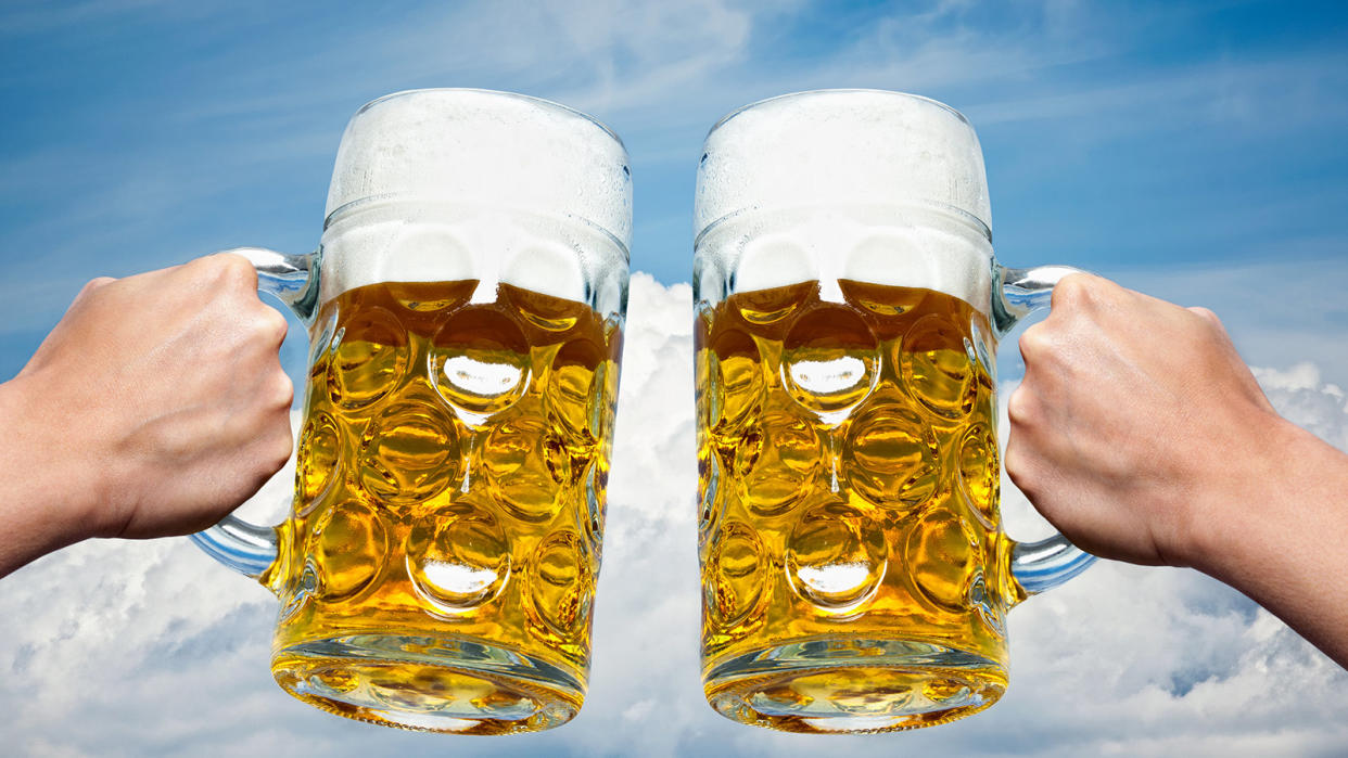  Two Full Beer Steins Clinking Together Against A Bright Blue Sky Backdrop. 