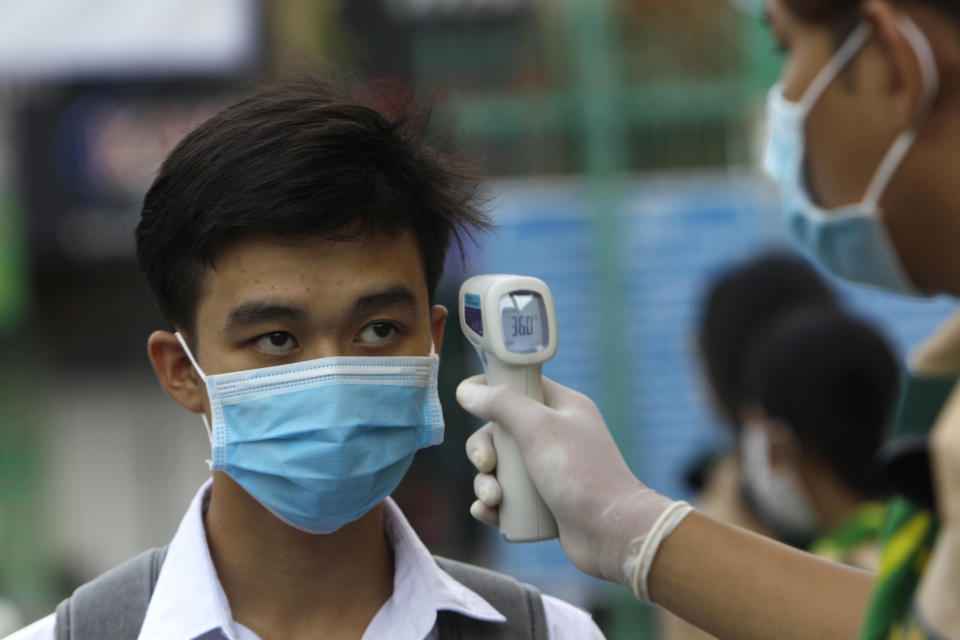 A school boy, left, has his temperature checked before he enters the Santhormok high school, in Phnom Penh, Cambodia, Monday, Nov. 2, 2020. Schools throughout Cambodia that had been shut in March because of the coronavirus crisis reopened Monday, but with limits on class sizes and hours.(AP Photo/Heng Sinith)