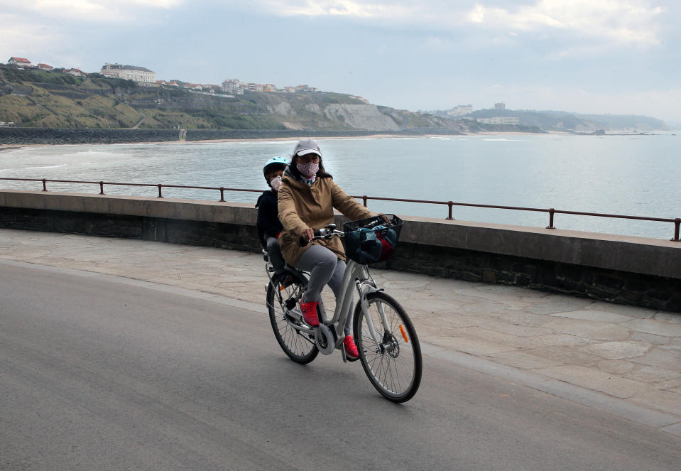 A family wearing face masks ride their bicycle during a nationwide confinement to counter the COVID-19, in Biarritz, southwestern France, Saturday April 11, 2020. The new coronavirus causes mild or moderate symptoms for most people, but for some, especially older adults and people with existing health problems, it can cause more severe illness or death. (AP Photo/Bob Edme)