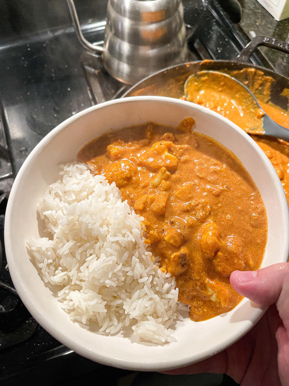 author holding bowl that's half steamed rice and half an orange curry with cauliflower