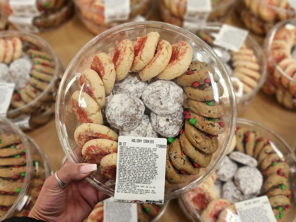 Hand holding plastic tray of holiday cookies with chocolate candies, red sprinkles, and powdered sugar