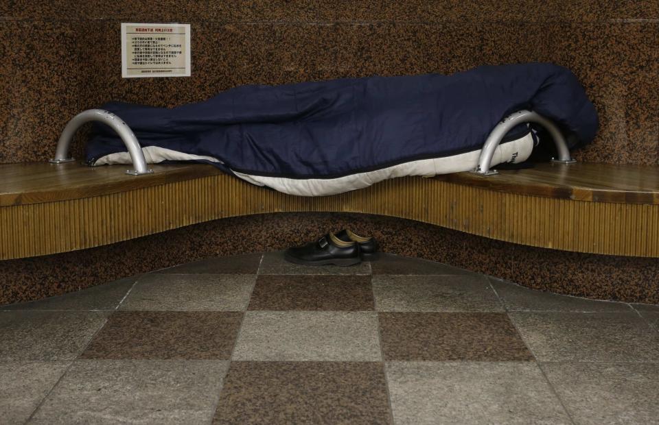 A homeless man snuggles in a sleeping bag on a bench at an underground passage near Sendai Station in Sendai