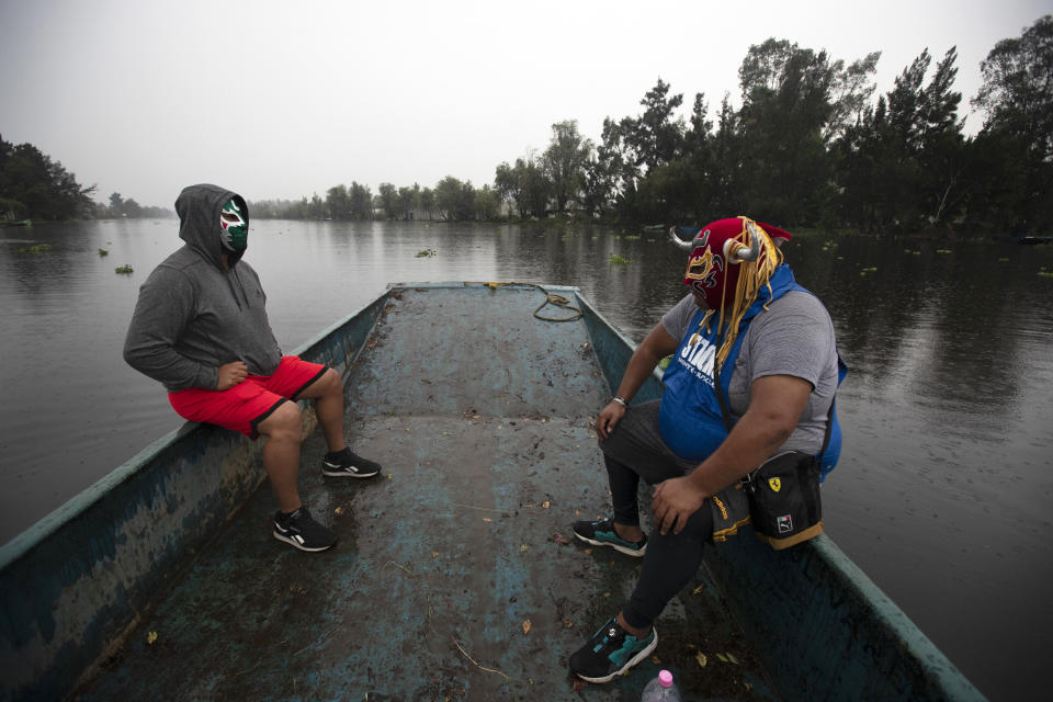 Los hermanos luchadores "Ciclónico", izquierda, y "Mister Jerry" viajan en una embarcación rumbo a su lugar de entrenamiento en los famosos canales de Xochimilco, en las afueras de Ciudad de México, la mañana del jueves 20 de agosto de 2020, en medio de la pandemia de COVID-19 que ha causado el cierre de arenas de Lucha Libre. (AP Foto/Marco Ugarte)