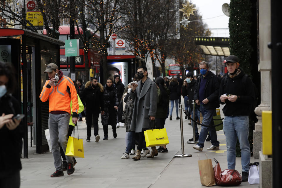 People carry shopping bags outside the Selfridges department store on Oxford Street, where shops are allowed to stay open under the newly placed Tier 3 restrictions for coronavirus in London, Wednesday, Dec. 16, 2020. London and some of its surrounding areas have been placed under Britain's highest level of coronavirus restrictions beginning at 00:01 local time on Wednesday as infections rise rapidly in the capital. Under Tier 3 restrictions, the toughest level in England's three-tier system, people can't socialize indoors, and bars, pubs and restaurants must close except for takeout. (AP Photo/Matt Dunham)