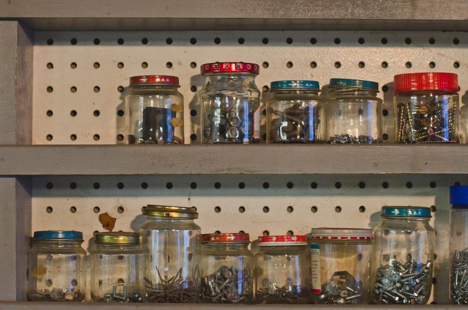 A row of wooden shelves in a old dusty work shop full of glass jars and screws in the old shop keeping everything stored.