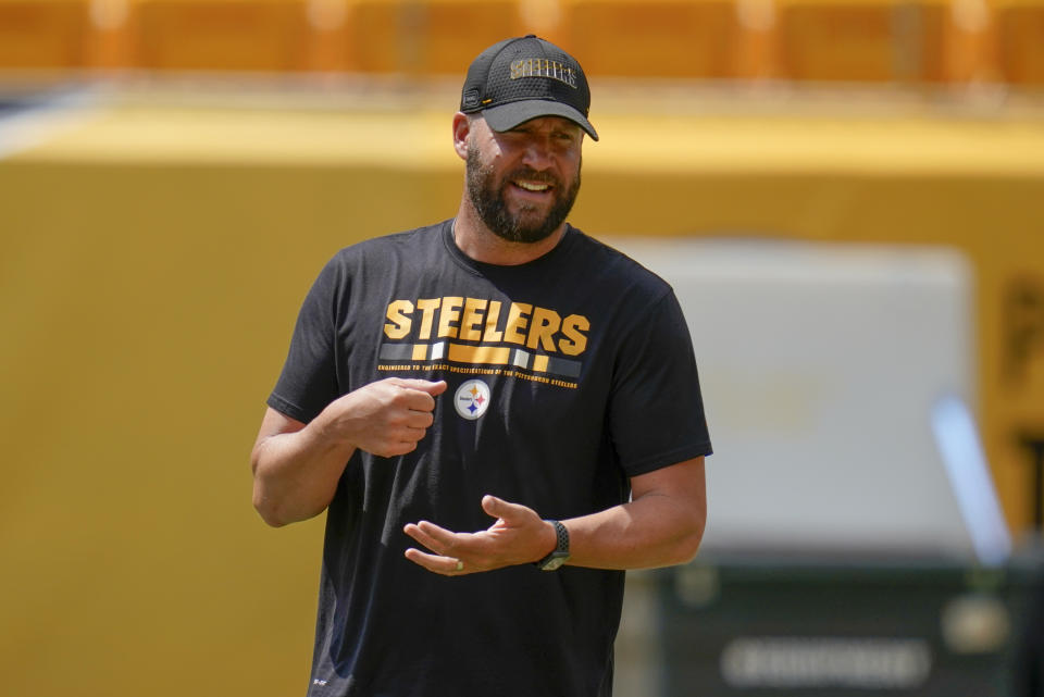 Ben Roethlisberger smiles while on the practice field wearing a black Steelers T-shirt and hat.