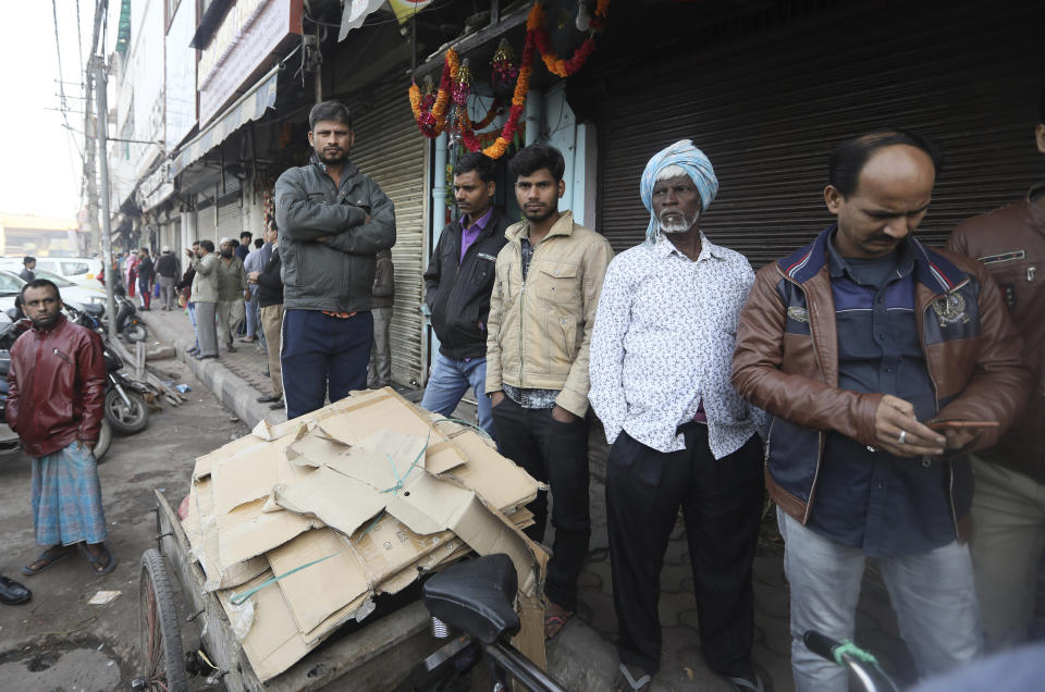 Daily laborers wait outside a market which was the scene of a devastating fire Sunday, in New Delhi, India, Monday, Dec. 9, 2019. Authorities say an electrical short circuit appears to have caused a devastating fire that killed dozens of people in a crowded market area in central New Delhi. Firefighters fought the blaze from 100 yards away because it broke out in one of the area's many alleyways, tangled in electrical wire and too narrow for vehicles to access. (AP Photo/Manish Swarup)