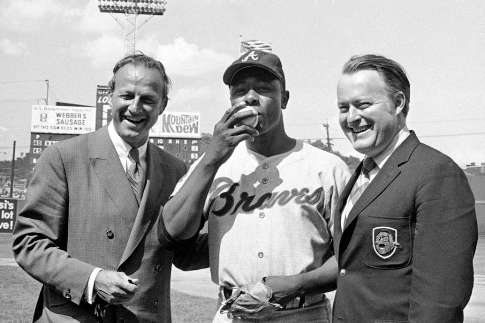 From May 17, 1970, Atlanta Braves' Hank Aaron, center, who became the ninth player in Major League history to get 3,000 hits, kisses a baseball alongside Famer Stan Musial and Braves owner Bill Bartholomay, in Cincinnati. Bartholomay, the former Braves owner who moved the team from Milwaukee to Atlanta in 1966, died Wednesday, March 25, 2020, at New York-Presbyterian Hospital, according to his daughter, Jamie. He was 91. Bartholomay sold the Braves to Ted Turner in 1976 but remained as chairman of the team's board of directors until 2003, when he assumed an emeritus role.