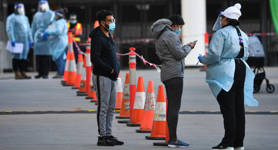 A healthcare worker is seen speaking to people waiting in line outside of a pop-up Covid19 testing facility outside of the LaCrosse apartment block in Docklands, Melbourne, Sunday, July 25, 2021. Source: AAP