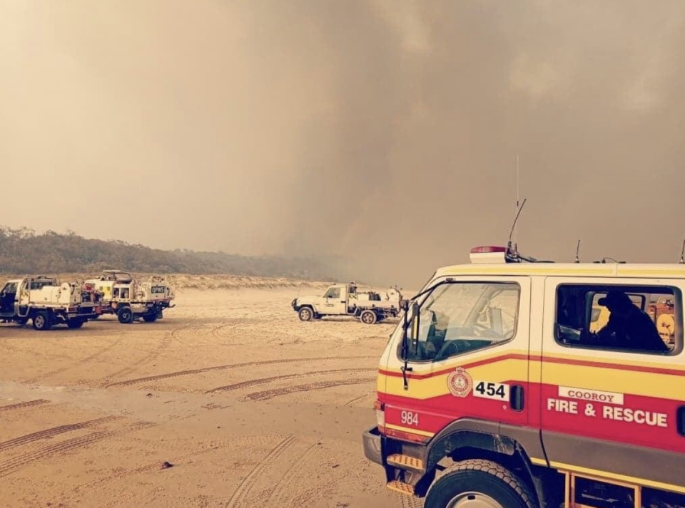 Fire trucks parked on the sand on Fraser Island as smoke looms overhead.