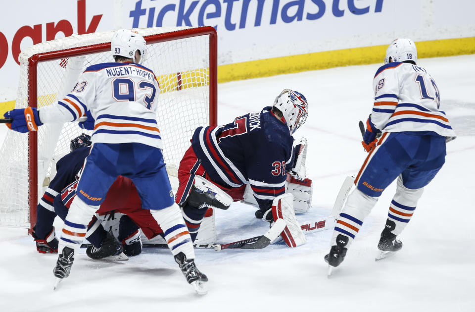 Edmonton Oilers' Zach Hyman (18) scores against Winnipeg Jets goaltender Connor Hellebuyck (37) in overtime of an NHL hockey game Tuesday, March 26, 2024, in Winnipeg, Manitoba. (John Woods/The Canadian Press via AP)