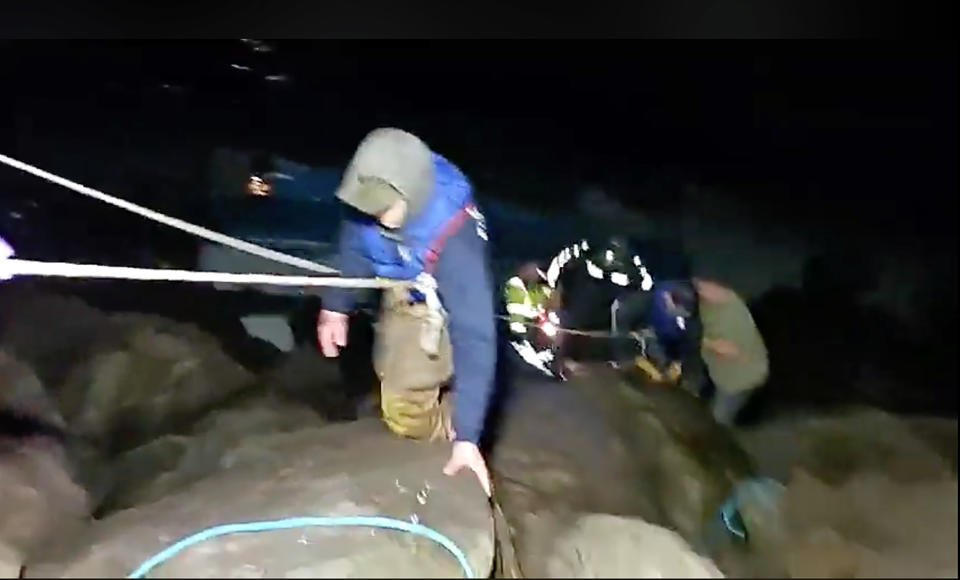 This photo from video provided by Rob Gensorek of Basin Tackle Charleston shows firefighters rescuing the crew from a capsized crab boat in the harbor at Coos Bay, Ore., late Tuesday evening, Jan. 14, 2020. Three men were in good condition early Wednesday after being cut from inside the hull of the capsized boat. The 38-foot (11-meter) Pacific Miner was flipped upside-down by large waves late Tuesday and then got caught on rocks in a jetty in Coos Bay as the tide went out. A U.S. Coast Guard helicopter on a routine training mission spotted the vessel and launched a rescue, the agency said in a news release. (Rob Gensorek of Basin Tackle Charleston via AP)