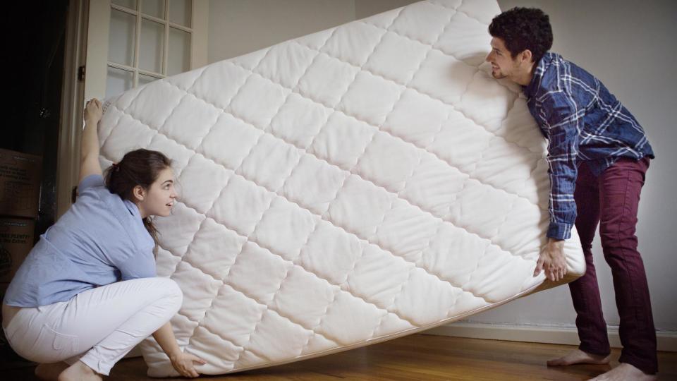 A man and a woman rotate a mattress after cleaning it