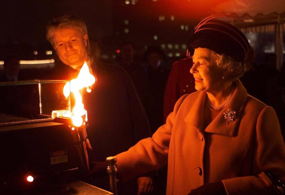 Britain's Queen Elizabeth II lights a beacon floating in the Thames as she travels by boat, Dec. 31, 1999 to the Millennium Dome at Greenwich. (AP Photo/Arthur Edwards, Pool)