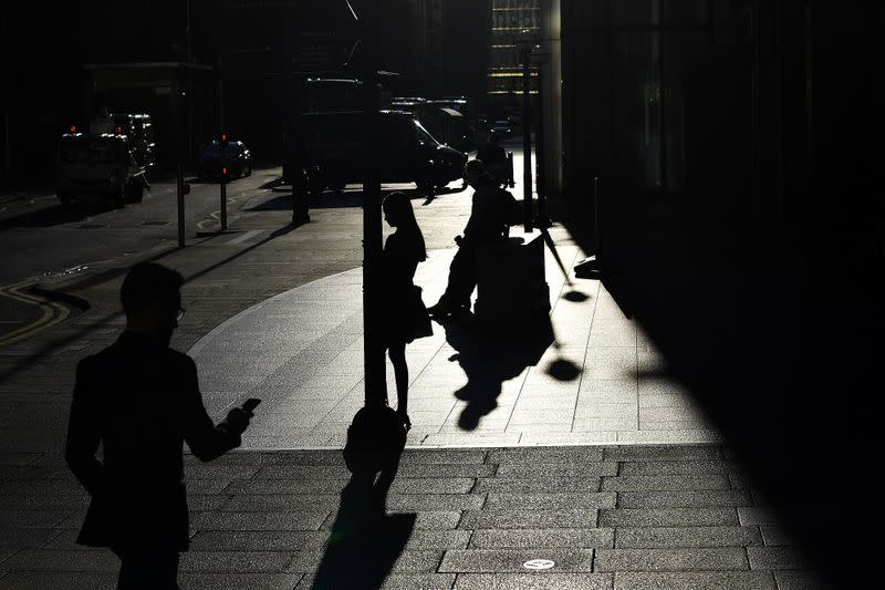 The early morning sun silhouettes commuters as they make their way through Canary Wharf in London