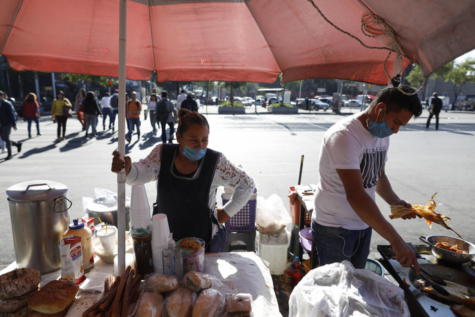Lourdes Sanvicente, 45, left, and a coworker wear protective face masks at the direction of the stand's owner, as they sell tamales, sandwiches, and pastries at a street stand in Mexico City, Wednesday, March 25, 2020. Sanvicente, who doubts the existence of the new coronavirus, says both she and her husband work as street food sellers, together earning 320 pesos (around $13.50) per day to support themselves and their five children. "There is no other option," she says, "I have to provide for my kids." (AP Photo/Rebecca Blackwell)