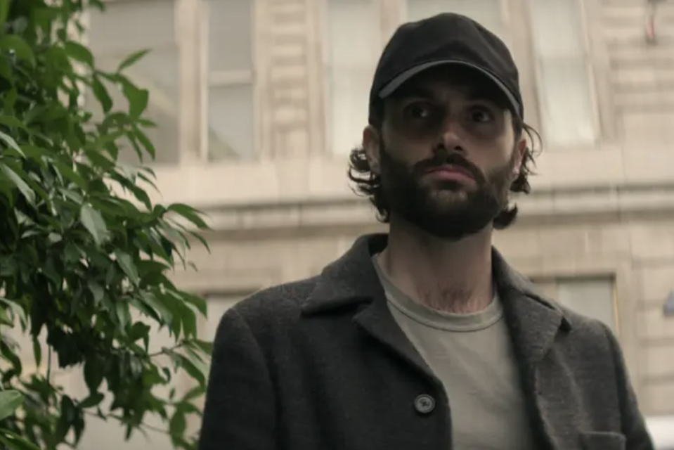 Penn Badgley in a beard and baseball cap standing outside