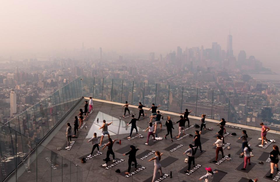 La gente asiste a una clase de yoga matutina en la plataforma de observación The Edge mientras una neblina causada por el humo de los incendios forestales que arden en Canadá se cierne sobre Manhattan (EPA)