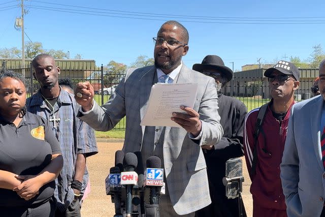 <p>Emily Palmer</p> Lawyer Malik Shabazz speaking at a Jackson, Miss. press conference March 18, heading into a week of sentencing hearings for the six former Mississippi officers. Standing behind him, wearing a cross necklace, is his client, Michael Jenkins, who was shot in the mouth by one of the officers in Jan. 2023.