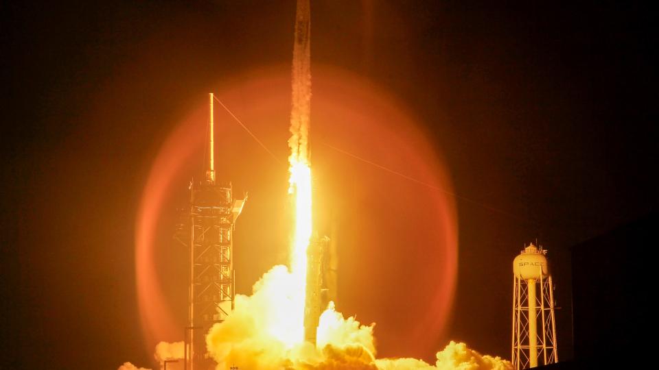 a white rocket lifts off at night above a plume of fire and smoke