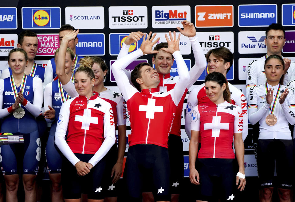 Switzerland's Stefan Bissegger, Stefan Kung, Mauro Schmid, Elise Chabbey, Nicole Koller and Marlen Reusser celebrate on the podium before being presented with their gold medals after winning the Team Time Trial Mixed Relay on day six of the 2023 UCI Cycling World Championships in Glasgow, Scotland, Tuesday, Aug. 8, 2023. (Jane Barlow/PA via AP)