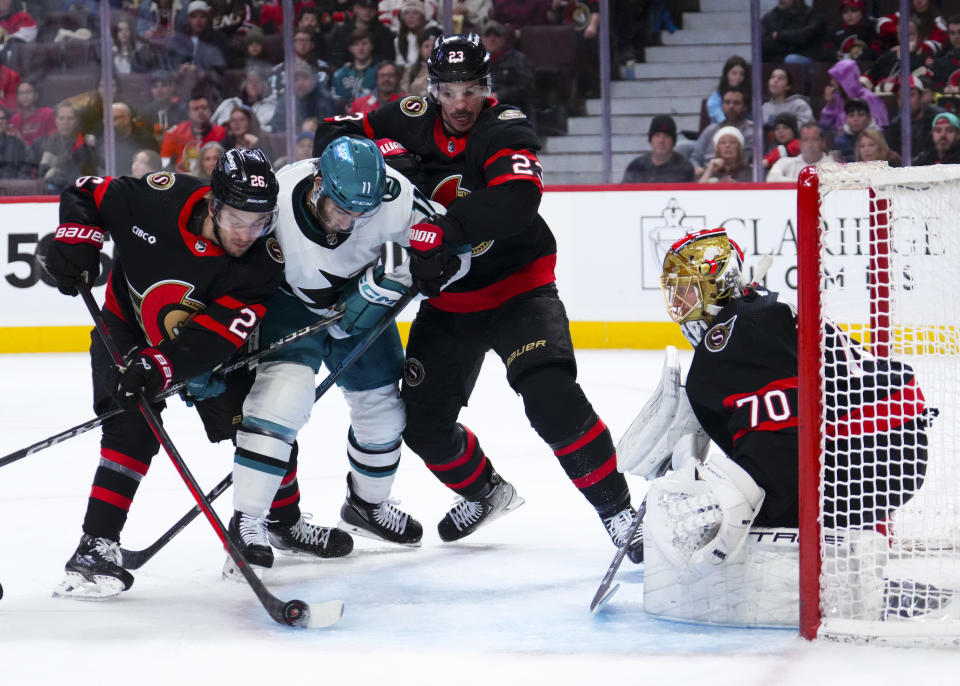 Ottawa Senators goaltender Joonas Korpisalo (70) keeps his eye on the puck as teammates defenseman Erik Brannstrom (26) and Travis Hamonic (23) hold off San Jose Sharks center Luke Kunin (11) during the first period of an NHL hockey game, Saturday, Jan. 13, 2024 in Ottawa, Ontario. (Sean Kilpatrick/The Canadian Press via AP)