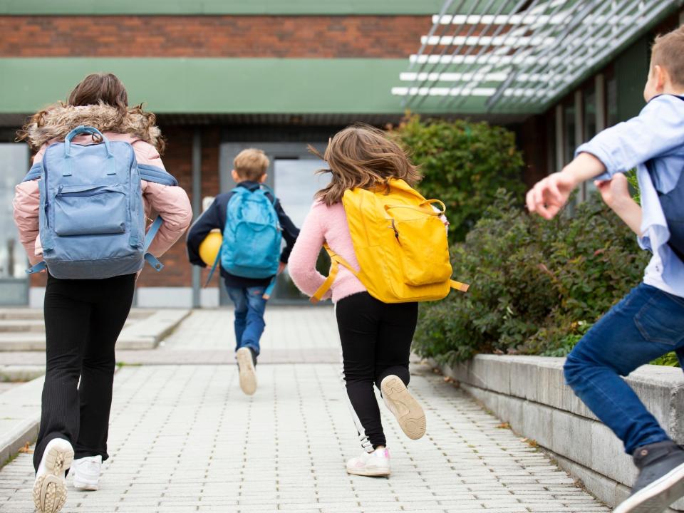 Kids wearing backpacks running toward a school.