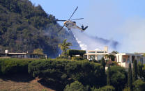 A Los Angeles County Fire Department helicopter makes a water drop as flames from a wildfire threaten homes on a ridgeline in the Pacific Palisades area of Los Angeles Monday, Oct. 21, 2019. (AP Photo/Reed Saxon)