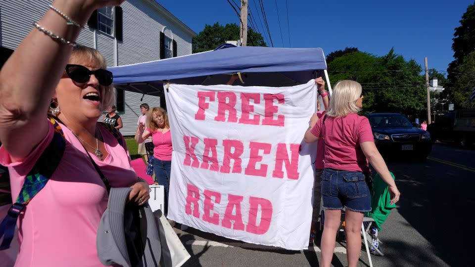 Eva Jenkins, of Bourne, Massachusetts, waves to passing cars as other supporters place a banner a block away from Norfolk Superior Court on Tuesday in Dedham, Massachusetts. - Steven Senne/AP