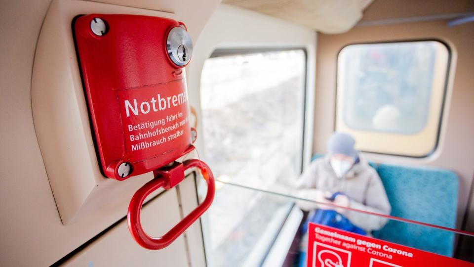 Ein Fahrgast mit Mund-Nasen-Schutz sitzt in einer Berliner S-Bahn hinter der Notbremse.