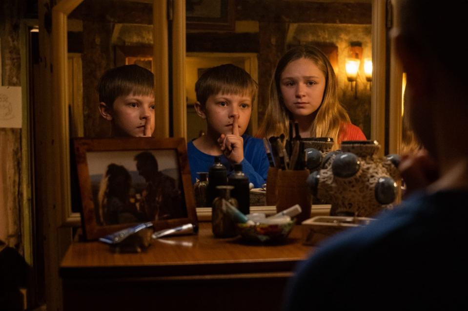 Two children, portrayed by Millicent Simmonds and Noah Jupe, are in front of a mirror with fingers over their lips, suggesting silence