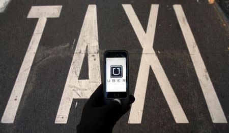 The logo of car-sharing service app Uber on a smartphone over a reserved lane for taxis in a street is seen in this photo illustration taken December 10, 2014. REUTERS/Sergio Perez/Illustration/Files