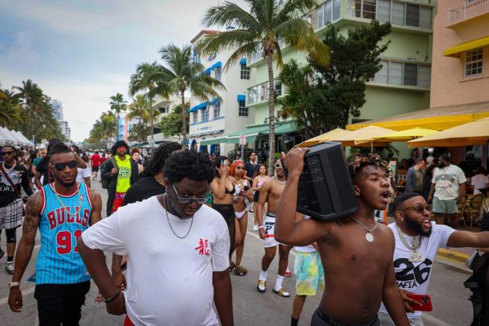 Spring breakers walk down Ocean Drive with a boom box on Sunday, March 19, 2023, in Miami.