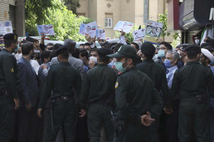 Supporters of former President Mahmoud Ahmadinejad hold his posters while he entered at Interior Ministry to register his name as a candidate for the June 18 presidential elections, as police officers prevent them to approach the ministry building in Tehran, Iran, Wednesday, May 12, 2021. The country's former firebrand president will run again for office in upcoming elections in June. The Holocaust-denying Ahmadinejad has previously been banned from running for the presidency by Supreme Leader Ayatollah Ali Khamenei in 2017, although then, he registered anyway. (AP Photo/Vahid Salemi)